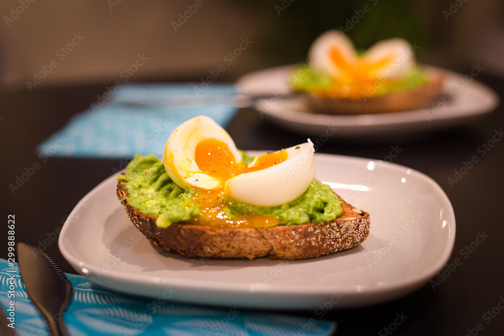 Two plates with a healthy breakfast of avocado on toast with a soft boiled egg. Two plates with a healthy breakfast of avocado on toast with a soft boiled egg.