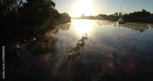 Aerial of golden sunrise at river with rawing boats. Golden fog moving at surface. Flying above water ascending to general view of riverbend. Volume light and flares. Mercedes city, Rio Negro, Uruguay photo