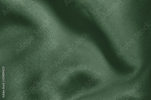 Dark green colored Background of soft draped fabric. Beautiful satin silk textured cloth for making clothes and curtains. Elegant textile texture.