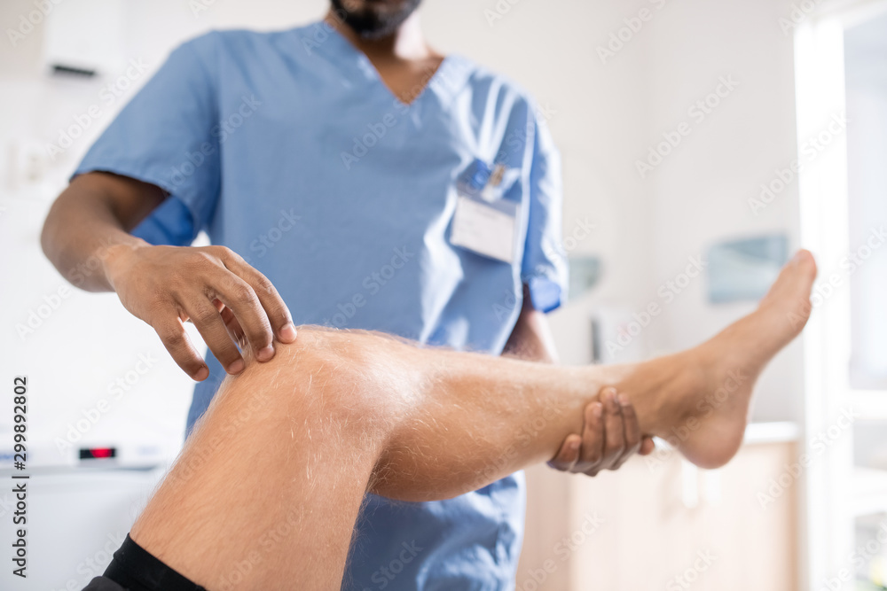 Contemporary mixed-race professional touching sick knee of his patient Contemporary mixed-race professional touching sick knee of his patient