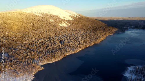 Aerial, reverse, drone shot, overlooking the frozen lake Kesankijarvi, forest and the Kesankitunturi fell, at sunrise, on a winter morning, in Pallas-yllastunturi national park, Lapland, Finland photo