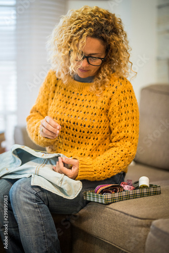 Adult housewife at home repairing clothes with cord - sailor and sew jeans jacket -beauiful young woman in activiy at home sitting on the sofa