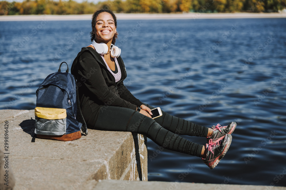 Cheerful Afro American lady with cellphone sitting by the river Cheerful Afro American lady with cellphone sitting by the river