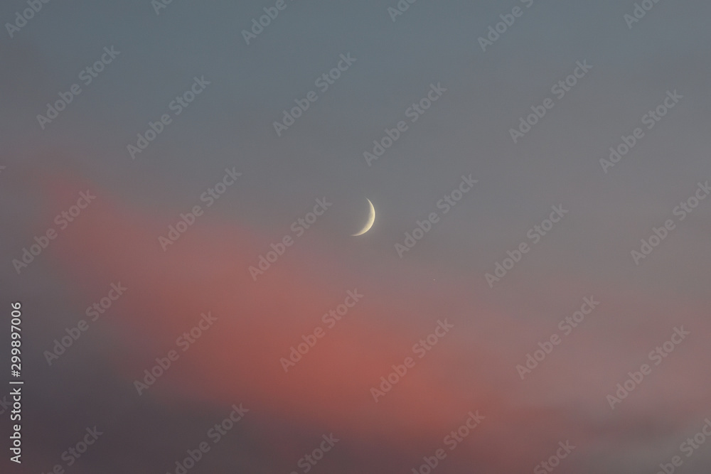 crescent moon among orange clouds at sunset