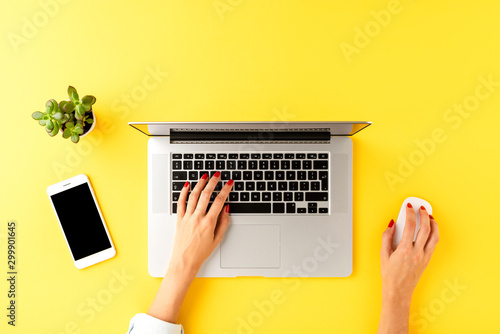 Businesswoman working on laptop. Office desktop with mobile phone and small succulent. Top view