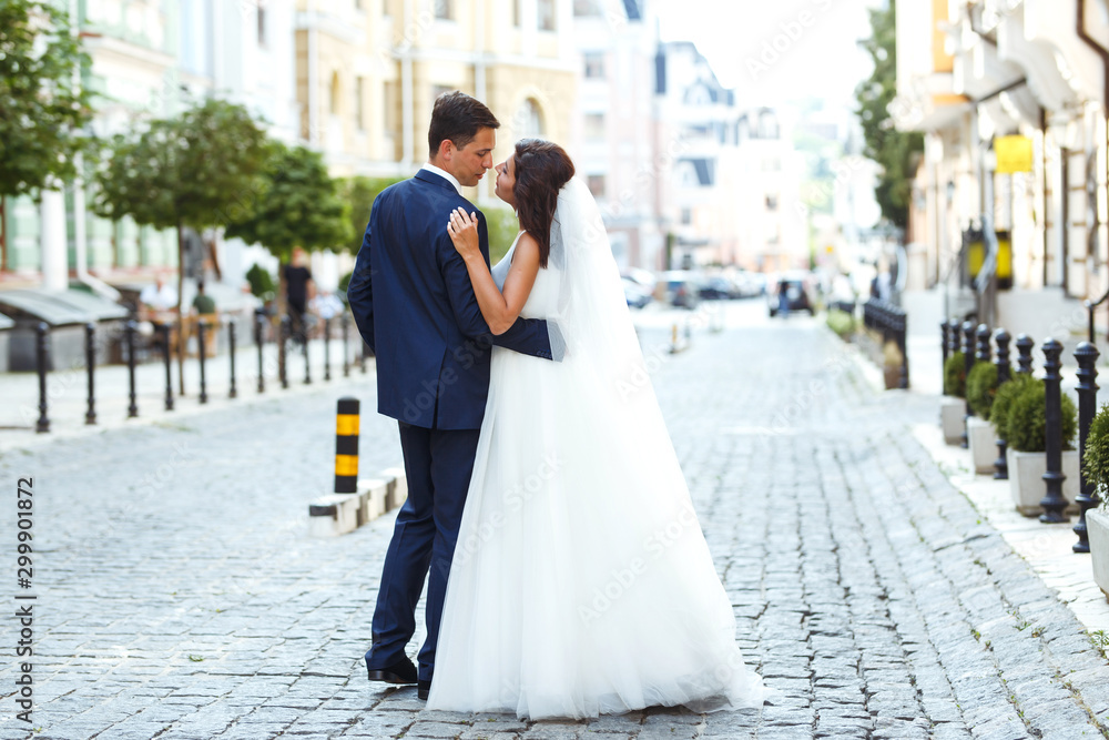 Fototapeta premium Gorgeous wedding couple walking in the city. Groom in a stylish suit and bride in a beautiful white dress, the couple is walking the streets of the city on their wedding day. Together. Wedding concept