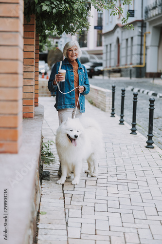 Smiling charming old woman walking her fluffy dog