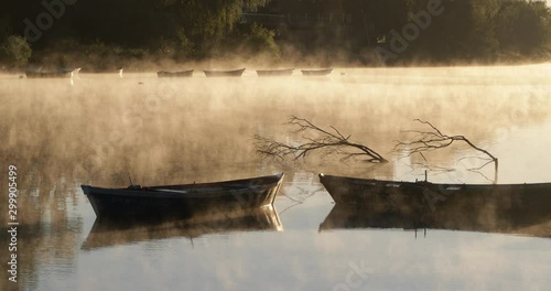 Golden foggy morning on a river, movement of mist over water surface passing through old rowing boats. Volume light and flares. Mysterious, calm scene. Rio Negro, Mercedes, Uruguay photo
