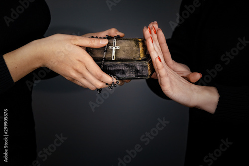 Woman gives two old Bibles and rosary to another woman which repels them by hands photo