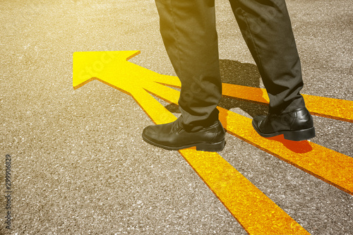 Business man in suit standing on floor with yellow arrow symbol. Top view. Selfie of feet in black leather shoes on street road background from above. Businessmen forward, start and success concept.