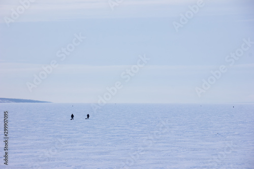 Fishermen walking on a frozen lake with ice fishing towards the horizon. Snowy field. © v1_one