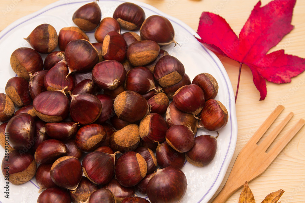 plate of chestnuts on wood and dried leaves plate of chestnuts on wood and dried leaves