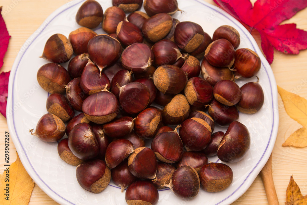 plate of chestnuts on wood and dried leaves plate of chestnuts on wood and dried leaves