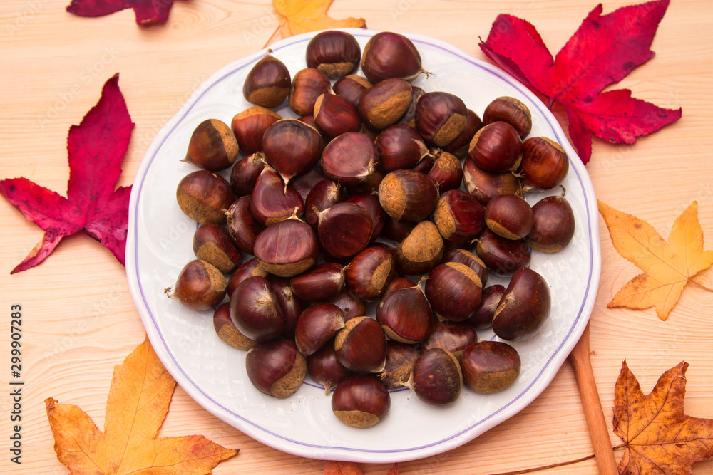 plate of chestnuts on wood and dried leaves plate of chestnuts on wood and dried leaves