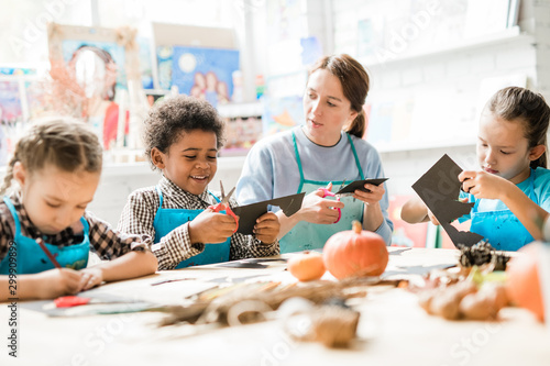 Multiracial schoolkids and teacher in aprons cutting out halloween decorations photo