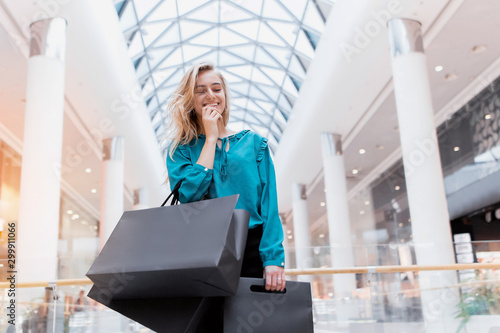 Black Friday. Discounts. Sales. Shopping A girl with packages and shopping smiles and enjoys new clothes. Black paper bags in hands on a blurred background of a shopping center.