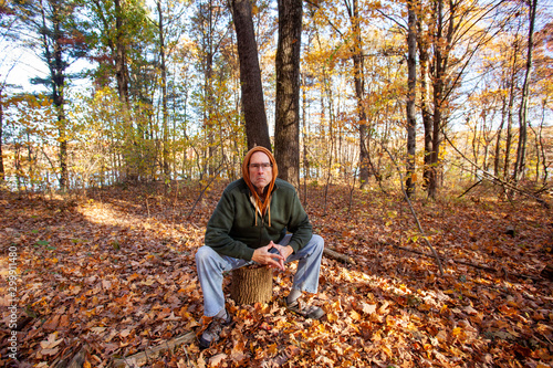 serious older man sitting on stump in woods