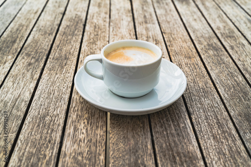 Hot foaming cappuccino in a white ceramic cup on a saucer stands on a table of wooden boards. photo