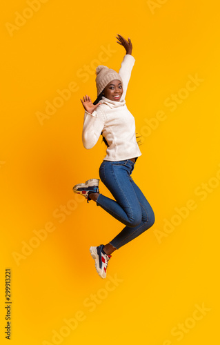 Carefree black girl jumping in the air over yellow background