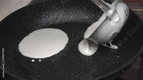 Ladle pours the dough for Russian pancakes onto a hot pan and the female hand distributes the dough to the pan. The process of making Russian traditional pancakes. Cooking delicious Russian pancakes. photo