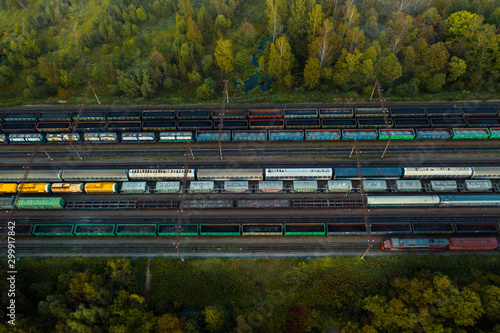 Aerial view of colorful freight trains on the railway station. Wagons with goods on railroad. Heavy industry. Industrial conceptual scene with trains. Top view from flying drone