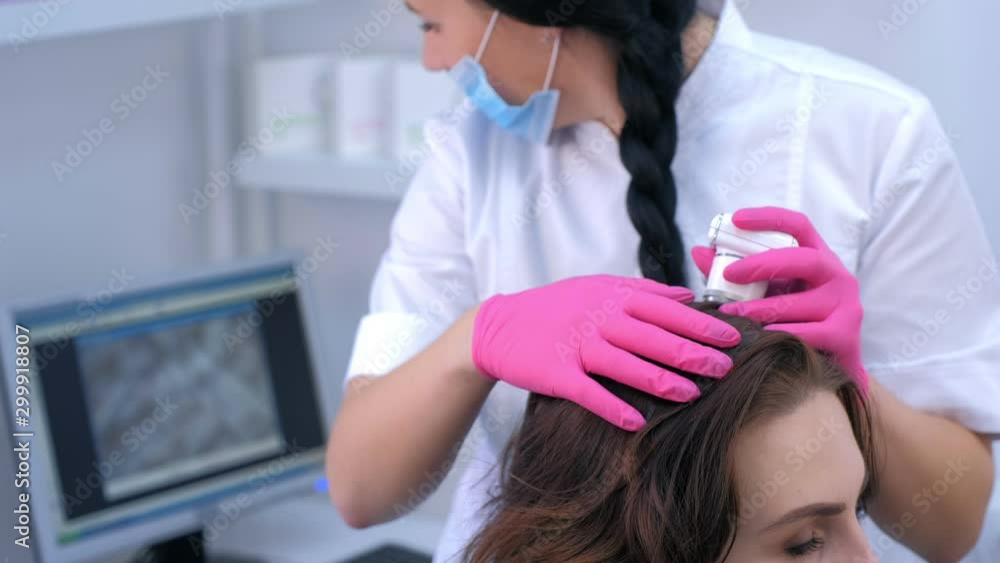 Doctor trichologist examines woman patient's hairs using trichoscope in