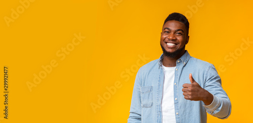 Happy african guy gesturing thumb up on yellow background