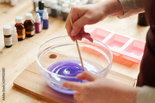 Hands of creative girl mixing lavender color with liquid soap mass in glassware