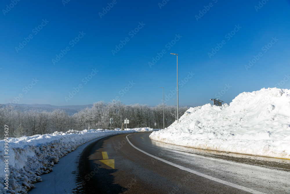 Snowy road scene in winter, with snowy trees, rocks and asphalt road.