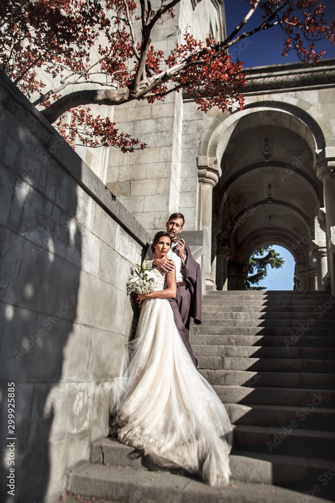 Happy groom look to beautiful bride wearing wedding dress and holding marriage bouquet in old street of the city with beautiful view. The couple hugging in love. Happy groom look to beautiful bride wearing wedding dress and holding marriage bouquet in old street of the city with beautiful view. The couple hugging in love.