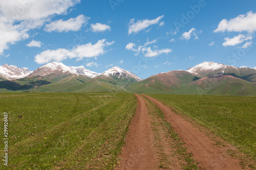 Dirt road leading to the mountains, mountains in the snow, in the summer