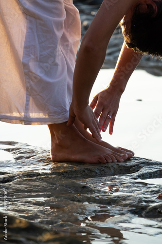 hands, feet and head of woman practicing yoga on the beach with white clothes