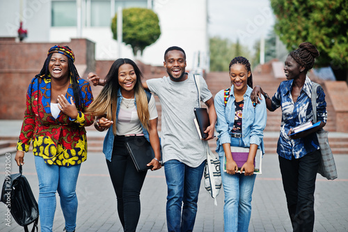 Group of five african college students spending time together on campus at university yard. Black afro friends studying. Education theme.