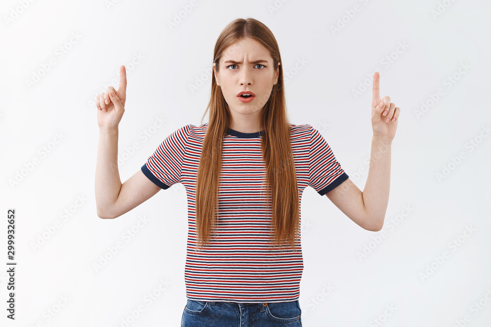 Distressed confused serious-looking caucasian woman in striped t-shirt, frowning puzzled and disappointed, squinting suspicious, standing bothered white background, pointing fingers up Distressed confused serious-looking caucasian woman in striped t-shirt, frowning puzzled and disappointed, squinting suspicious, standing bothered white background, pointing fingers up