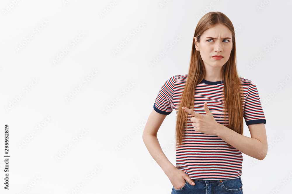 Obraz premium Hesitant and suspicious, unsure young fair-haired woman in striped t-shirt, frowning, squinting uncertain, pointing left and peek skeptical, standing confused white background, see something strange