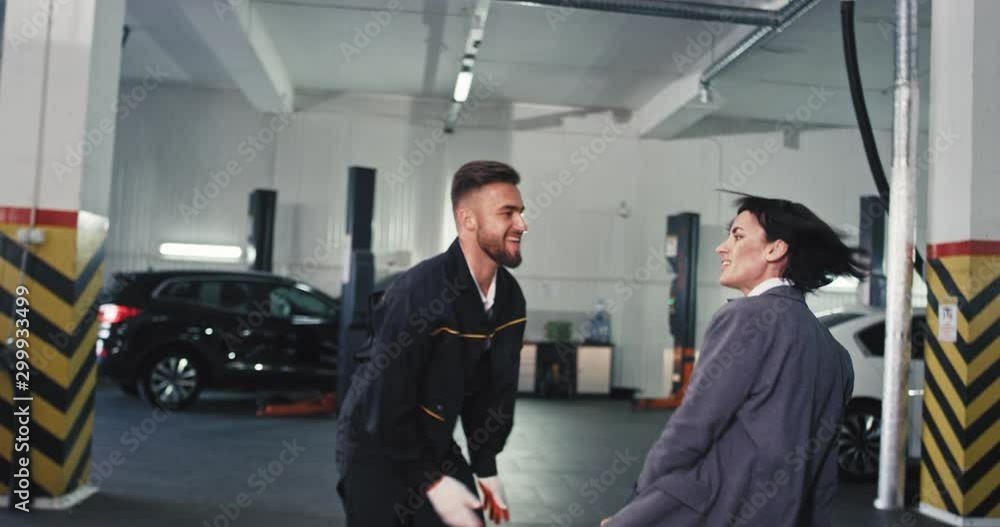 After a hard work day two service auto workers take a break and dancing excited in front of the camera mechanic and his manager woman After a hard work day two service auto workers take a break and dancing excited in front of the camera mechanic and his manager woman
