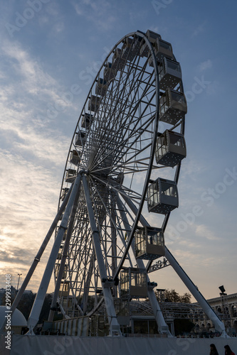 Ferris wheel on a square in a big city on an autumn evening on the background of cloudy sky. Tourist attraction and entertainment. Vertical