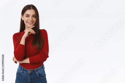 Girl thinking about interesing concept, have good idea. Attractive brunette woman in red blouse, touching chin and smiling sly, having creative plan, standing thoughtful or pensive, white background photo