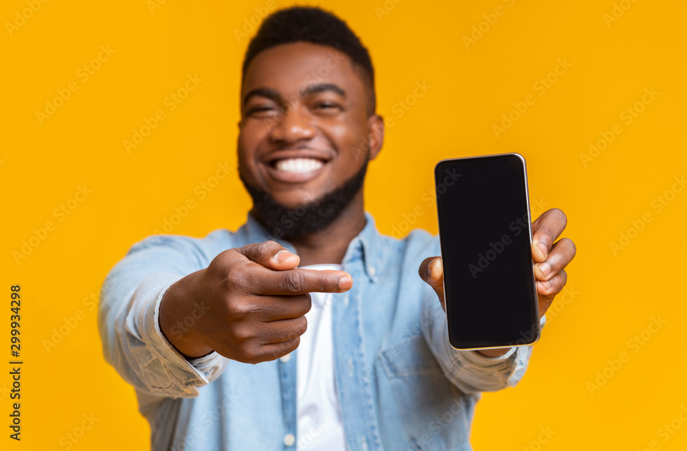 Cheerful african guy pointing at smartphone with black screen Cheerful african guy pointing at smartphone with black screen