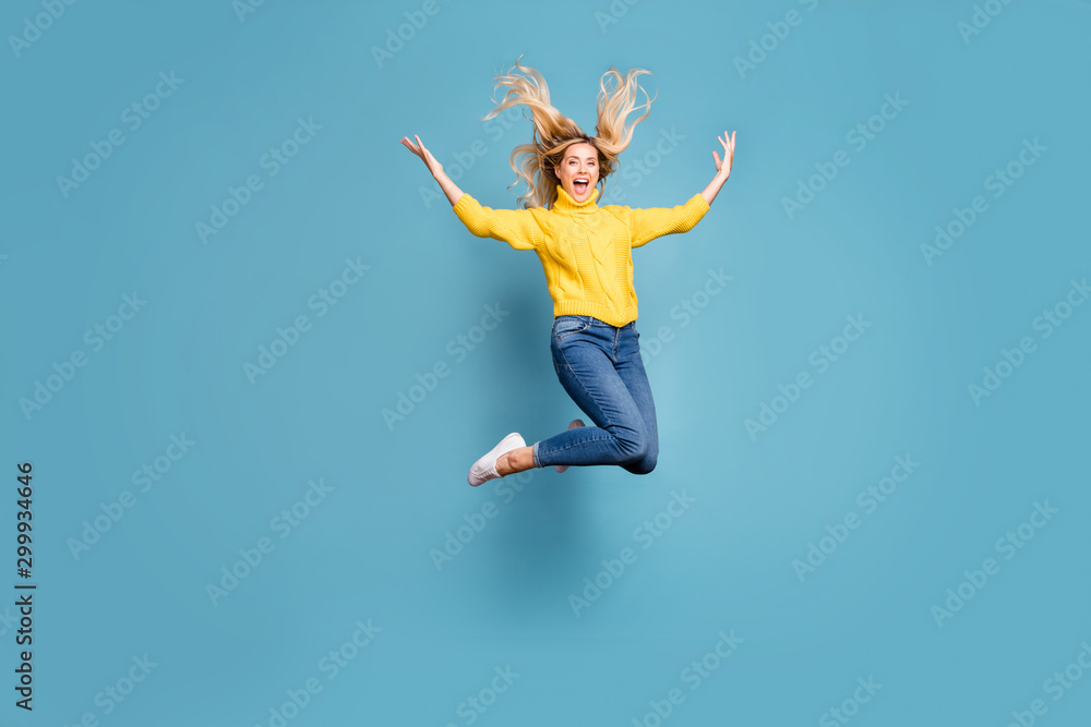 Full body photo of crazy lady jumping high enjoy warm autumn breeze hairdo flying cheerful person wear knitted yellow pullover jeans isolated blue color background