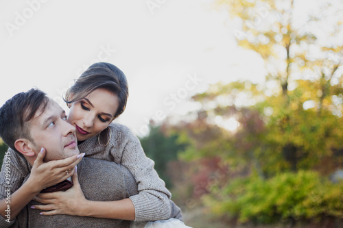 Portrait wedding couple wearing sweater, dress and suit, resting in the nature. The groom hug the bride with love against the beautiful vie of the sun and leaves. Man picked uo a woman in his arms.