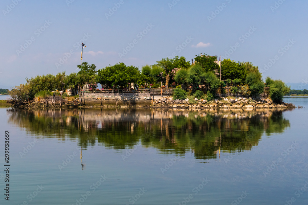 Grado, Italy - June 28th, 2019: One of the many little islands in the lagoon of Grado that offer a nice weekend escape in a small house and garden surrounded by the water or serve as fishermens huts.