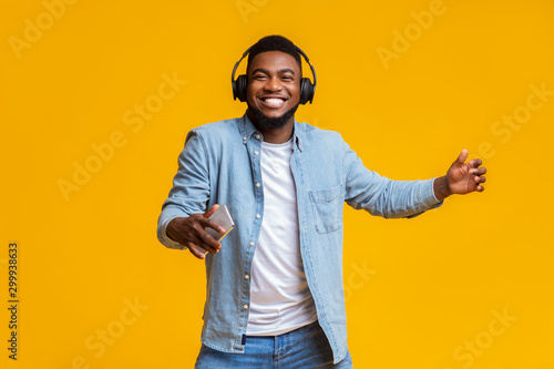 Cheerful guy in headphones listening music on smartphone and dancing