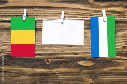 Hanging flags of Mali and Sierra Leone attached to rope with clothes pins with copy space on white note paper on wooden background.Diplomatic relations between countries.