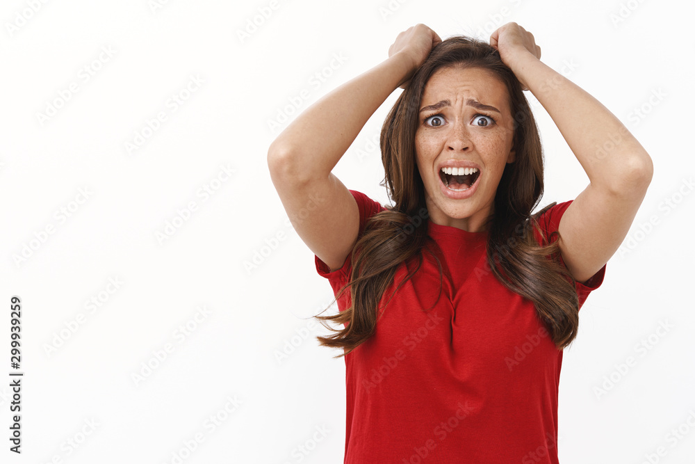 Remourse, sorrow and failure concept. Upset shocked panicking brunette woman in red t-shirt pull hair out of head, scream disappointed, stuck in troublesome bad situation, white background
