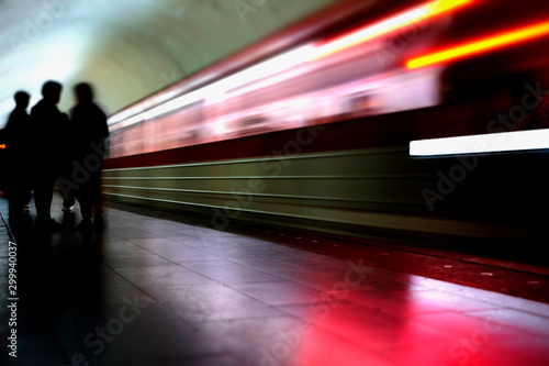 Silhouette of passengers on the platform while the train is arriving. Blurred image of moving train and silhouettes of people on the platform.