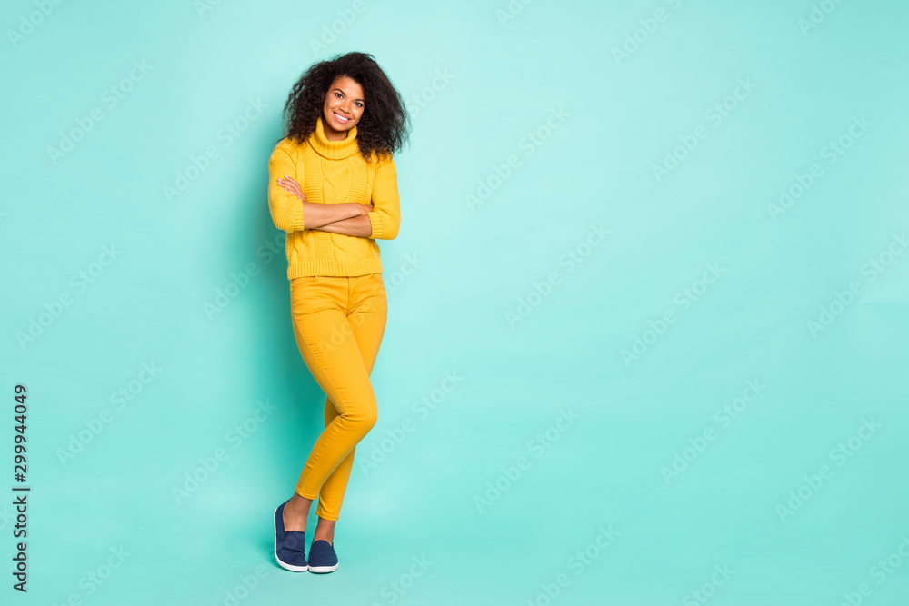 Full length photo of amazing dark skin lady holding arms crossed cool street look wear yellow knitted pullover trousers isolated blue teal color background Full length photo of amazing dark skin lady holding arms crossed cool street look wear yellow knitted pullover trousers isolated blue teal color background