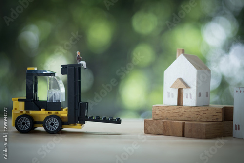 Miniature banker sit on yellow forklift go to move home to another location.