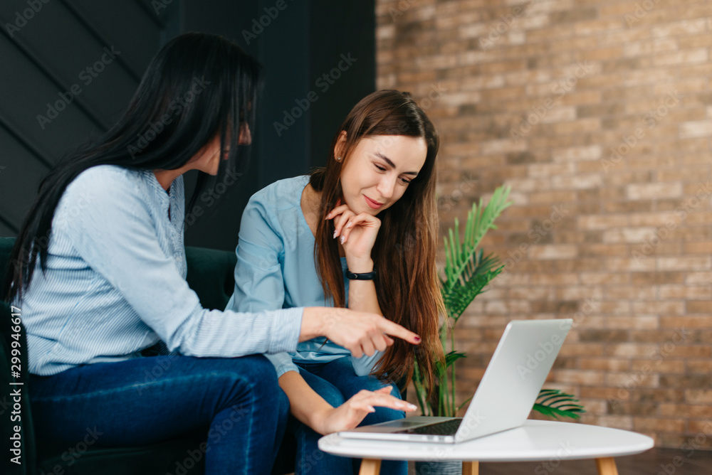 Young woman points her friend at laptop screen Young woman points her friend at laptop screen
