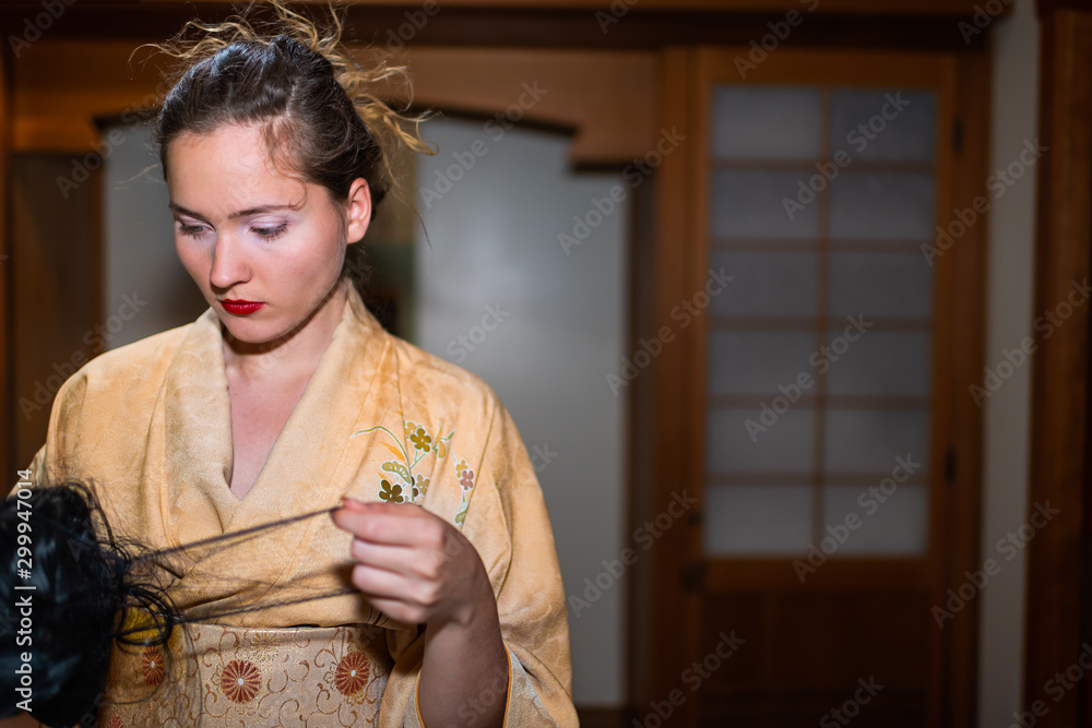 Young woman in kimono getting ready by traditional wooden door holding black wig in Japanese house home Young woman in kimono getting ready by traditional wooden door holding black wig in Japanese house home